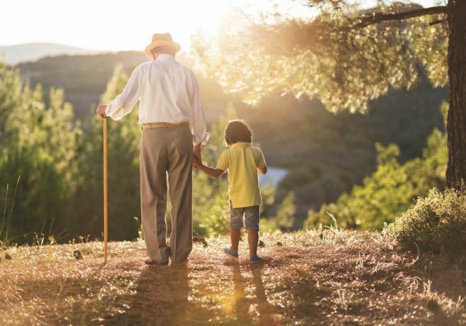 изглед отзад или дядо с бастун, който държи ръката на малкия си внук, докато е на разходка