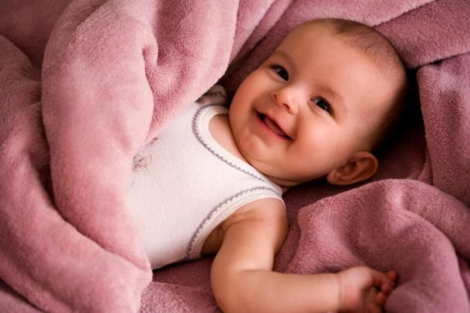 портрет на бебе в бяла тениска, усмихнато и увито в меко розово одеяло
