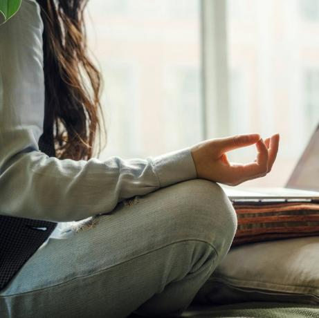 азиатска жена на средна възраст в сини дънки, седнала на леглото в поза за йога пред лаптоп отдалечена работа вкъщи онлайн пазаруване в период на карантина