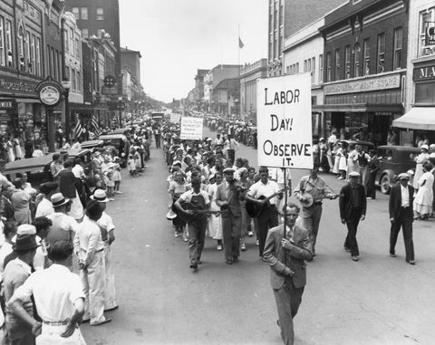 парад на деня на труда през 1934 г. с хора, които се разхождат по улицата, докато държат знаци, докато тълпата наблюдава от тротоарите