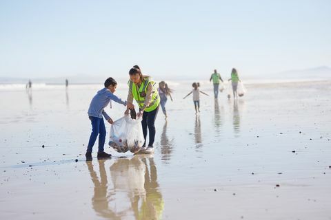 Майка и син доброволци почистват отпадъци на слънчев, мокър пясъчен плаж