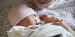 новородено момиче с розова шапка, завито в одеяло с майка, гледана от брадичката надолу в болнична рокля, която я държи