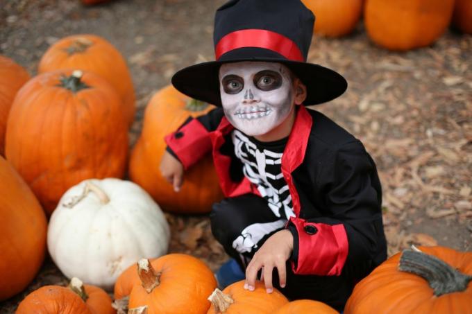 Хелоуин деца, които си играят на трик или лакомство момче в костюм за Хелоуин на скелет с шапка и смекинг между оранжеви тикви Хелоуин деца