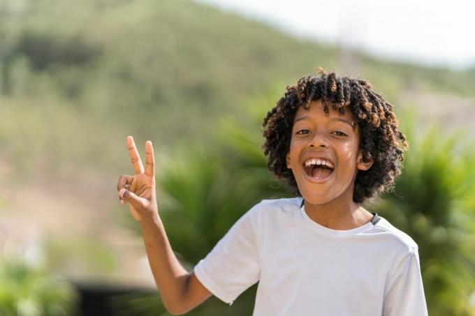 10-годишно афро-американско момче се смее на глас, докато прави знака за мир