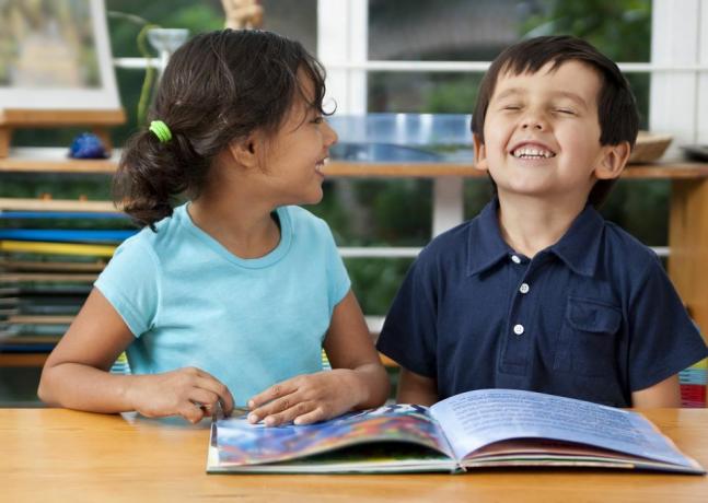 две смеещи се деца, които се наслаждават на книга в училище