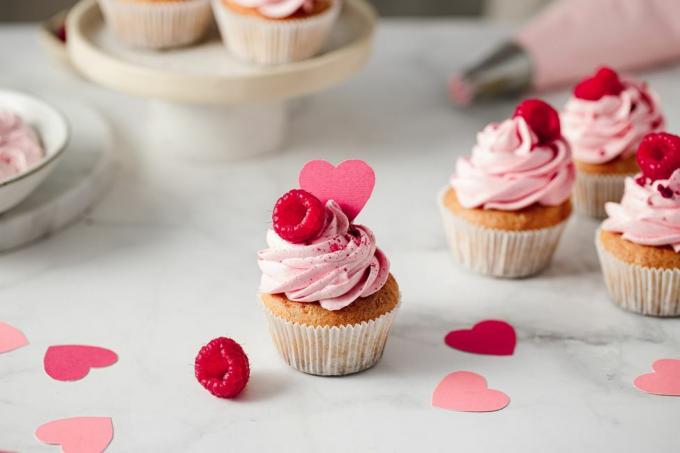прясно приготвени малинови кексчета на кухненския плот вкусно изглеждащи розови кексчета с топинг от малини и хартиено сърце