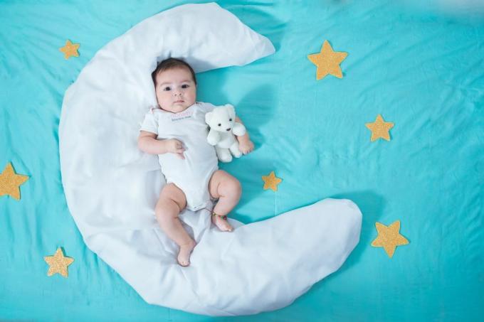 красиво латино момиченце, на два месеца, лежащо върху бял чаршаф във формата на луна с жълти звезди от всяка страна и син чаршаф отдолу