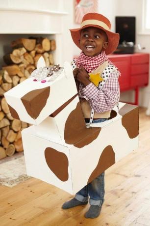малко момче, облечено като каубой с каубойска шапка и карирана риза и бандана с картонен кон около кръста