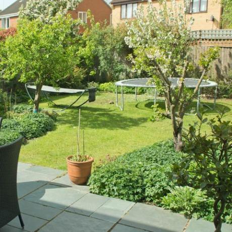 задна градина в английски крайградски имот със столове и маса върху вътрешен двор с плочи и батут и хамак на моравата на заден план