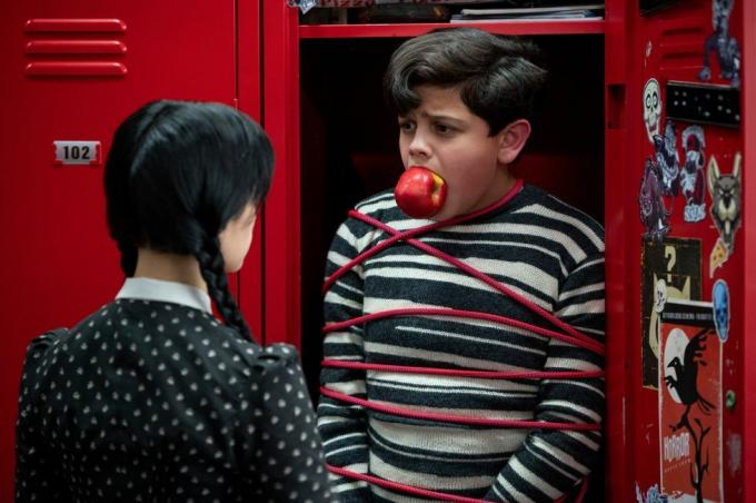 момиче гледа момче, вързано в шкафче с ябълка в устата