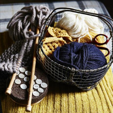 топки от синя и бяла вълна в малка телена кошница, дървени игли за плетене, копчета, поставени върху жълта оребрена плетена тъкан, текстура