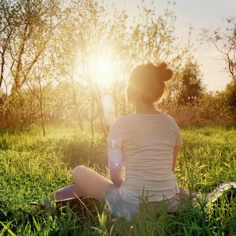 млада жена, седнала в поза за йога, наслаждавайки се на залез сред природата