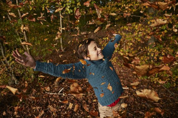 весело момче, наслаждаващо се сред падащи есенни листа