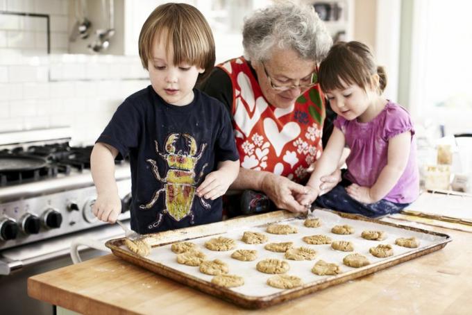 баба и двама малки внуци пекат внучката поставя тесто върху бисквитен блат с помощта на баба