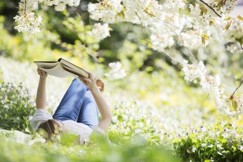 Жена четене на книга под цъфтящо дърво